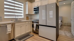 A modern kitchen with white cabinets, a stainless steel refrigerator, a gas stove, and a window with blinds. - California Midterm Rental With Fenced Yard! (Tracy)