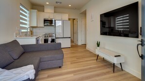 A modern living room with a grey sofa, a white bench, and a flat-screen TV mounted on the wall. - California Midterm Rental With Fenced Yard! (Tracy)