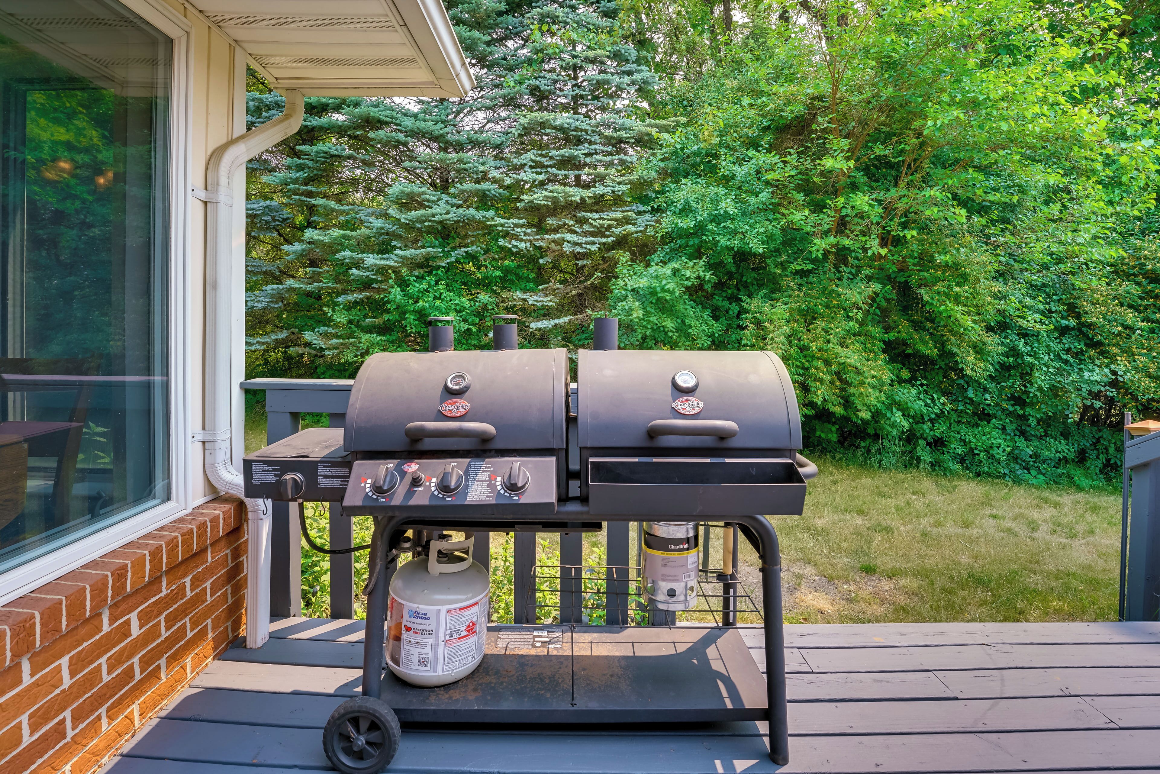 Ein Grill mit zwei Räuchern und einer Propangasflasche auf einer Terrasse.
