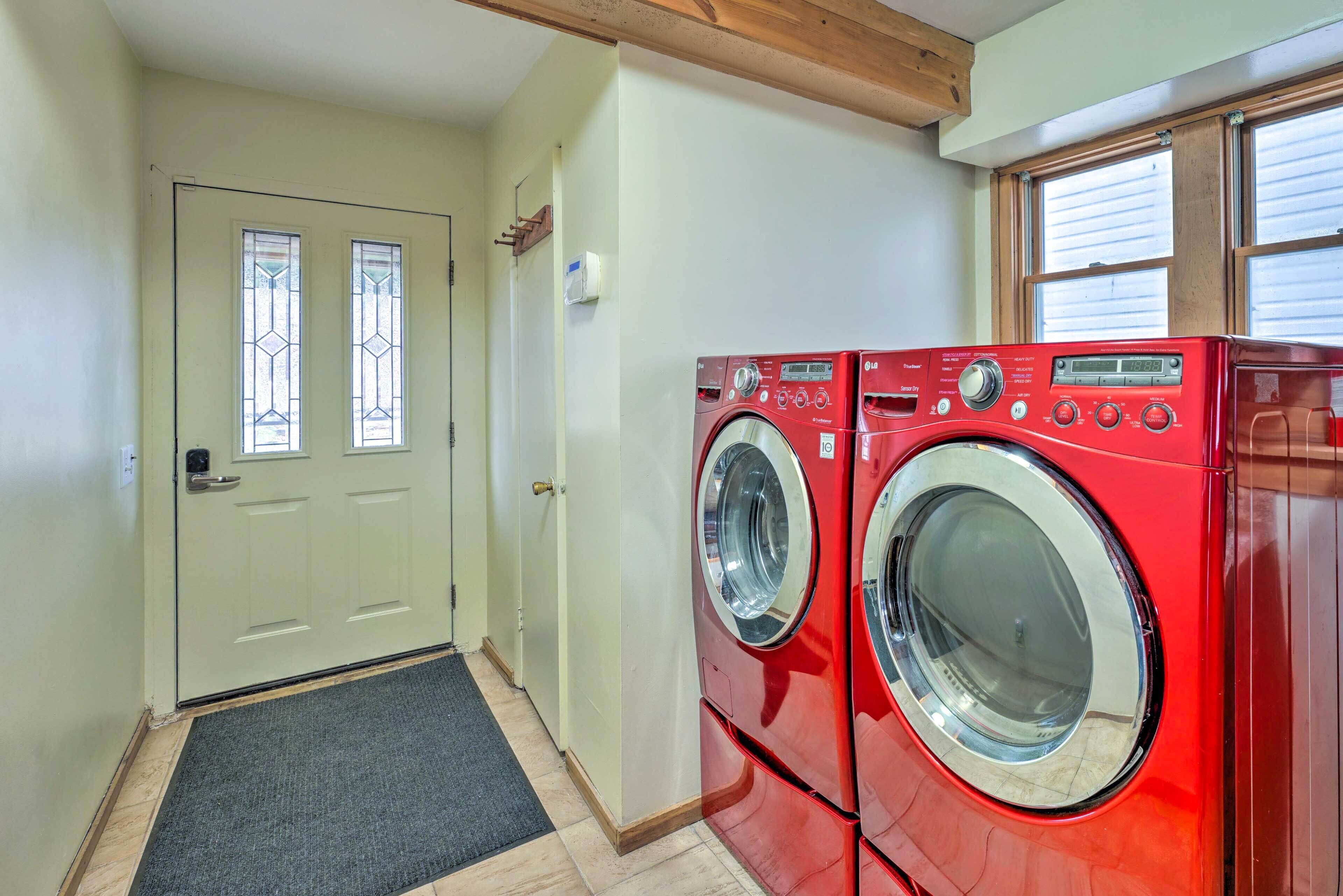 A laundry room with two red front-loading washing machines, a door with a glass panel, and a window with blinds.
