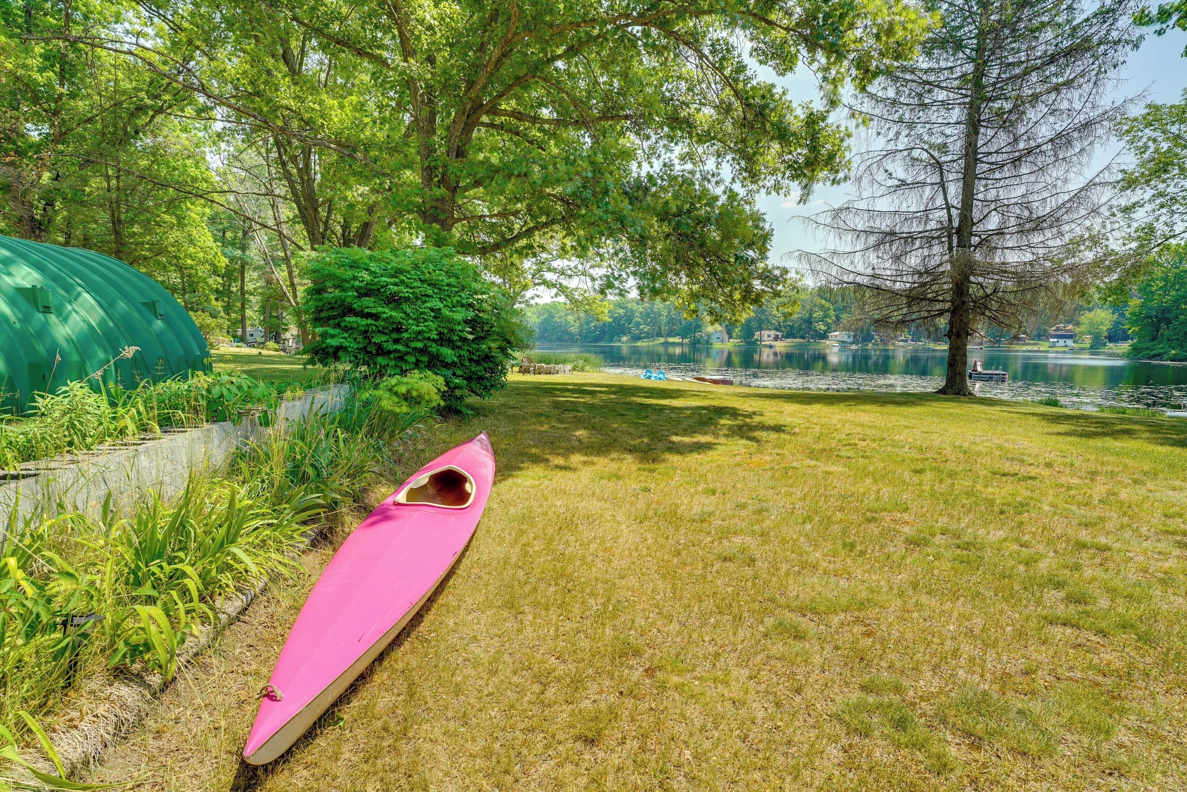 A grassy area with a pink canoe, a green tent, and a lake with boats in the background.