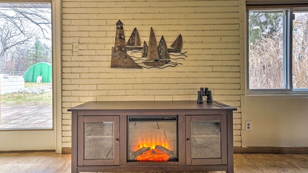 Un caminetto con vetro frontale, un mobiletto in legno con piano metallico e un'opera d'arte appesa alla parete raffigurante vele.