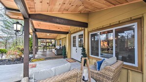 A covered patio area with wicker furniture, a small table, and a lantern. - Otto Home w/ Fire Pit, Tree House & Hot Tub! (Otto)