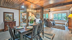 A spacious living room with a wooden ceiling, a dining area with a wooden table and chairs, a fireplace, and a large window. - Otto Home w/ Fire Pit, Tree House & Hot Tub! (Otto)
