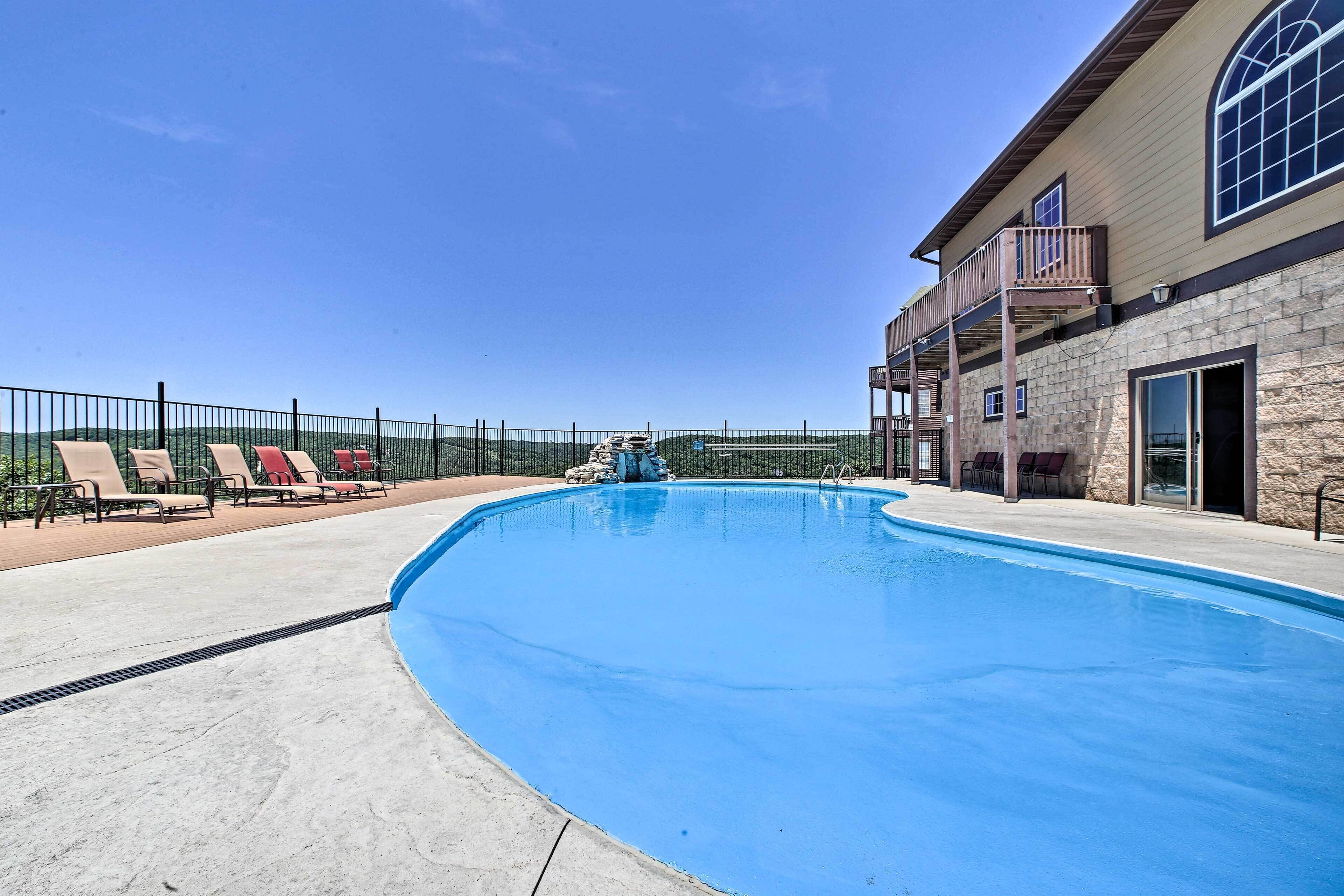 A swimming pool with lounge chairs, a stone building with a balcony, and a clear blue sky.
