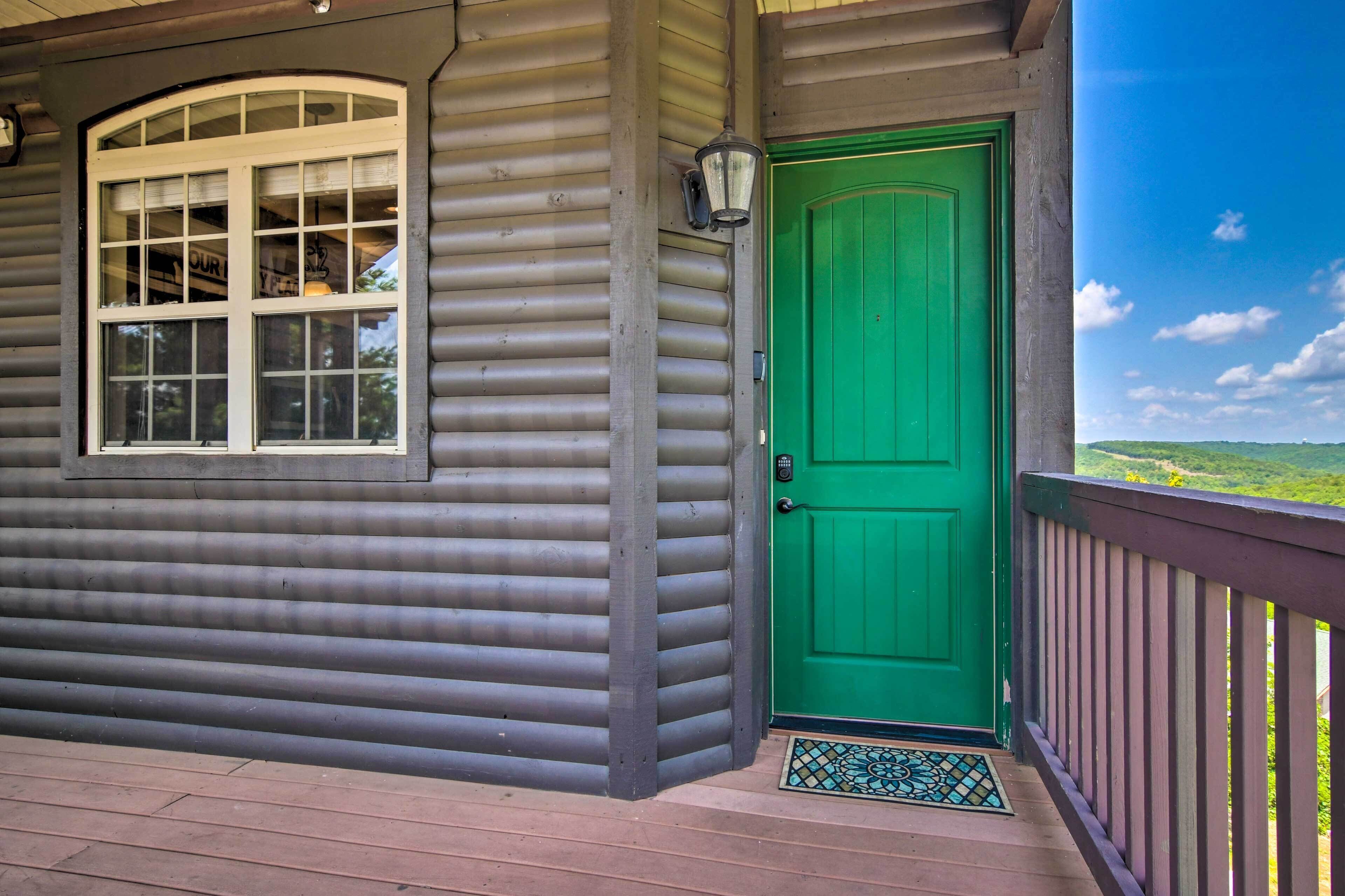 A wooden cabin with a green door, a window with a view, and a porch with a railing.