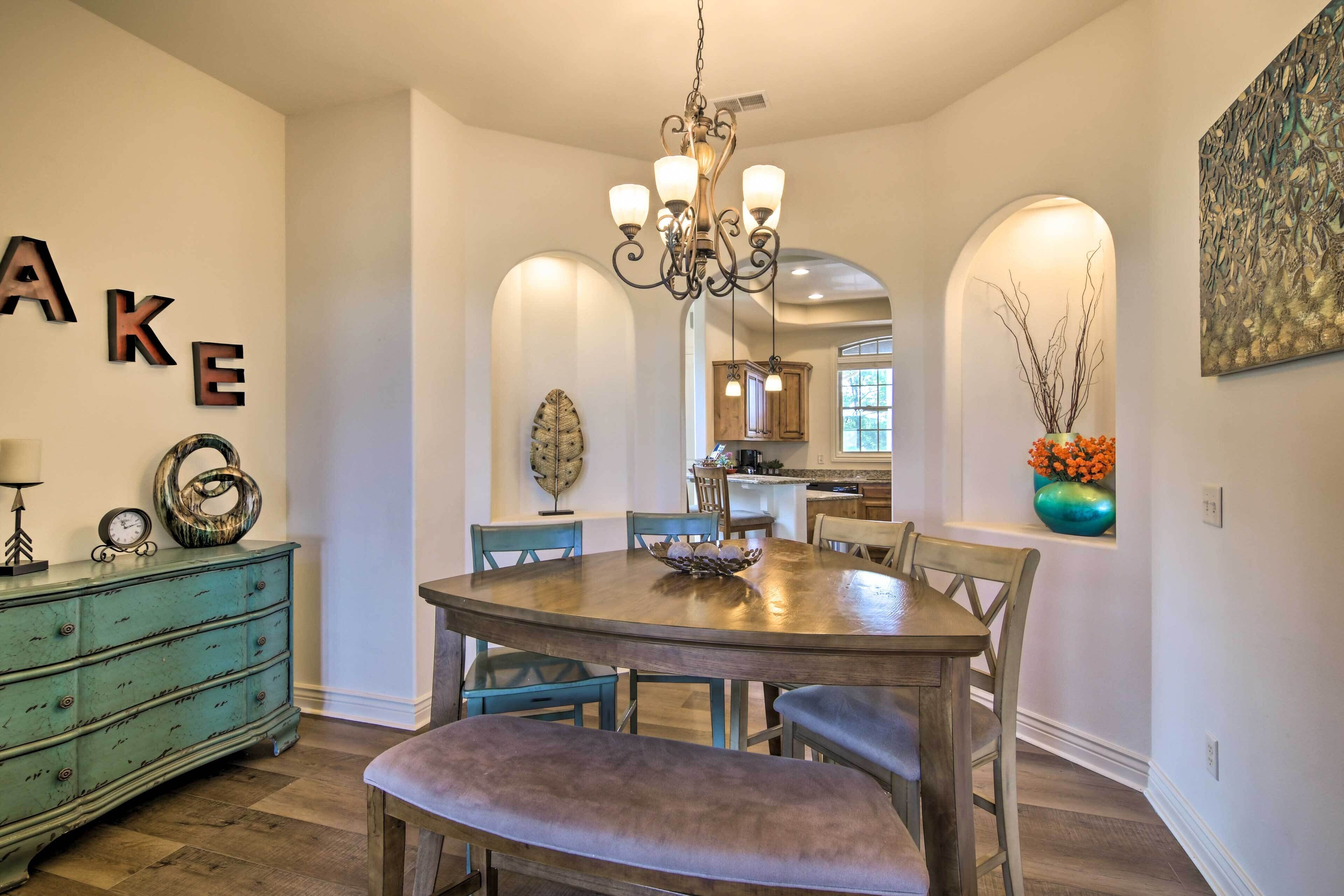 A dining area with a wooden table, blue chairs, and a chandelier. There is a green dresser with decorative items and a wall with letters spelling "AKE".