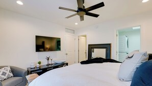 A modern bedroom with a large bed, a ceiling fan, a flat-screen TV, and a door leading to a bathroom. - High-end & Luxe Scottsdale Gem w/ Pool & Yard (Scottsdale)