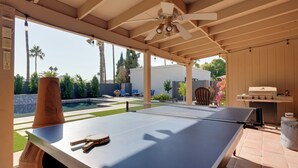 A ping pong table with a ceiling fan, a barbecue grill, and a pool in the background. - High-end & Luxe Scottsdale Gem w/ Pool & Yard (Scottsdale)