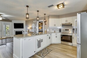A modern kitchen with white cabinetry, a central island, stainless steel appliances, pendant lighting, and a fireplace. - Foley Beach Cottage w/ Waterfront Backyard! (Foley)