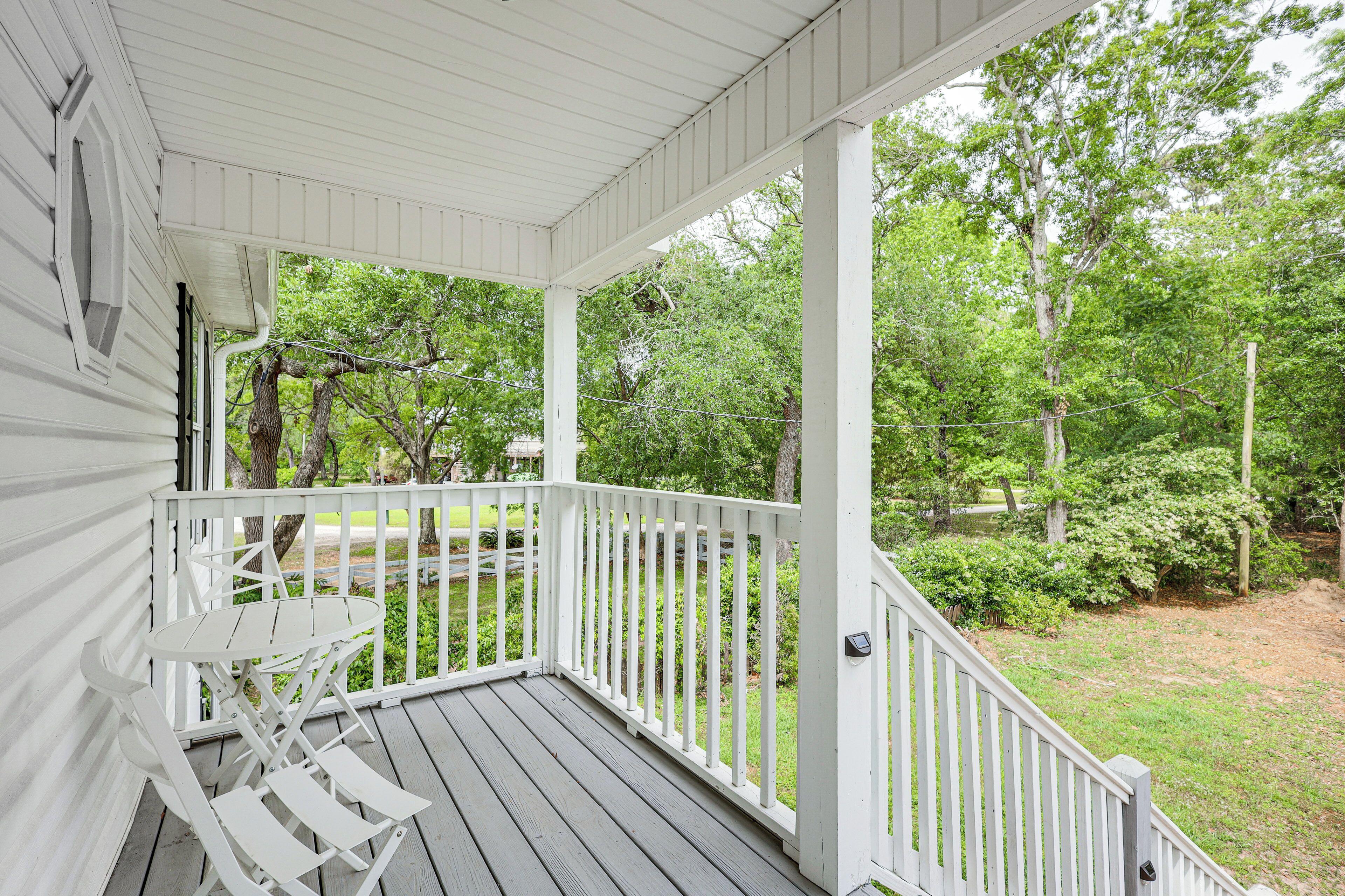 A covered porch with a white railing, a table, and chairs.