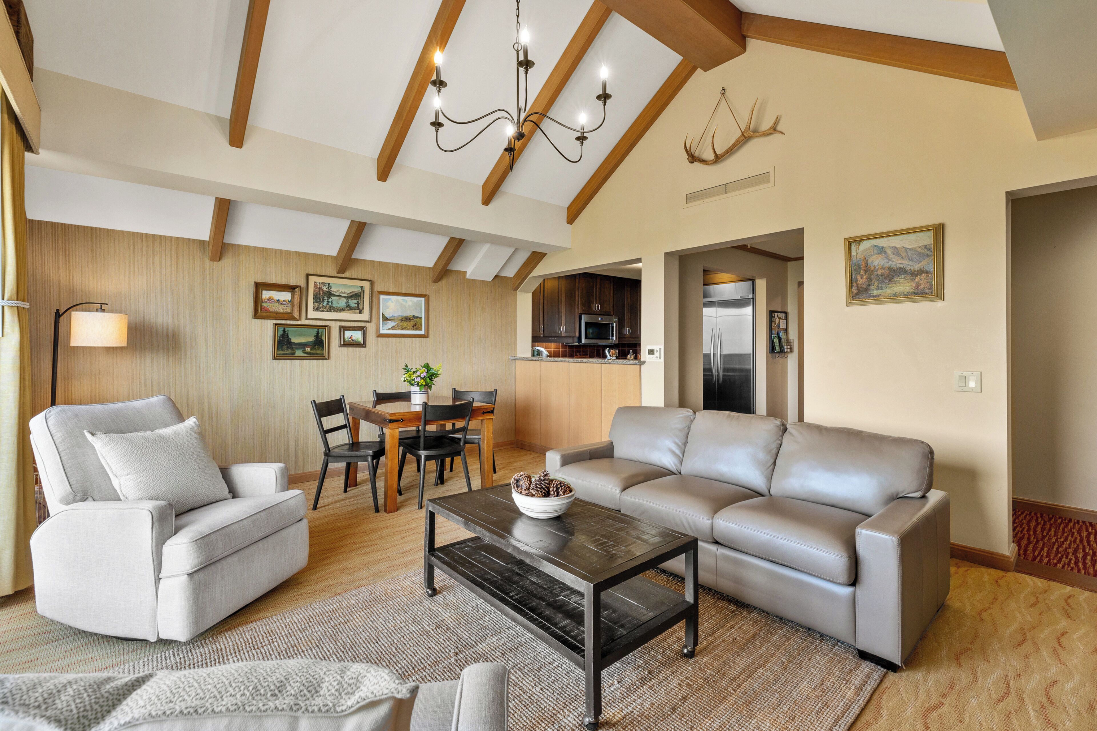 A living room with a sofa, armchairs, a coffee table, and a chandelier. There is a dining area with a table and chairs.