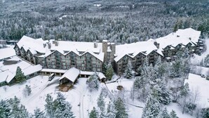 Um grande lodge com vários edifícios, rodeado por árvores cobertas de neve e montanhas ao fundo.