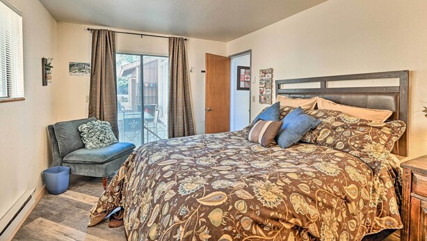A bedroom with a large bed, a chair, a window with curtains, and a door. - Relaxing Deck & Grill: Pinetop Townhome! (Pinetop)