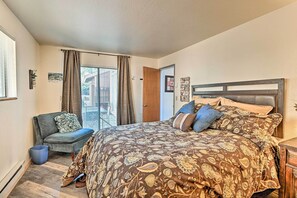 A bedroom with a large bed, a chair, a window with curtains, and a door. - Relaxing Deck & Grill: Pinetop Townhome! (Pinetop)