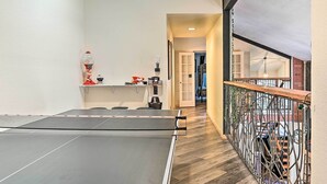 A ping pong table in a room with a wooden floor, a staircase with a metal railing, and a door leading to another room. - Relaxing Deck & Grill: Pinetop Townhome! (Pinetop)
