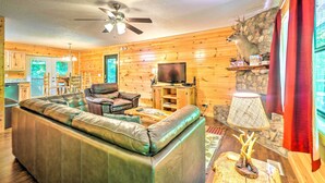 A cozy cabin interior with a leather sofa, a television, and a stone wall. - Cozy Gatlinburg Hideaway w/ Private Hot Tub! (Gatlinburg)