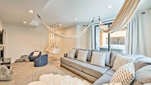 A modern living room with a grey sofa, patterned cushions, a white furry rug, and a hammock. - Newly-built Lakeside Gem w/ Community Perks! (Huntsville)