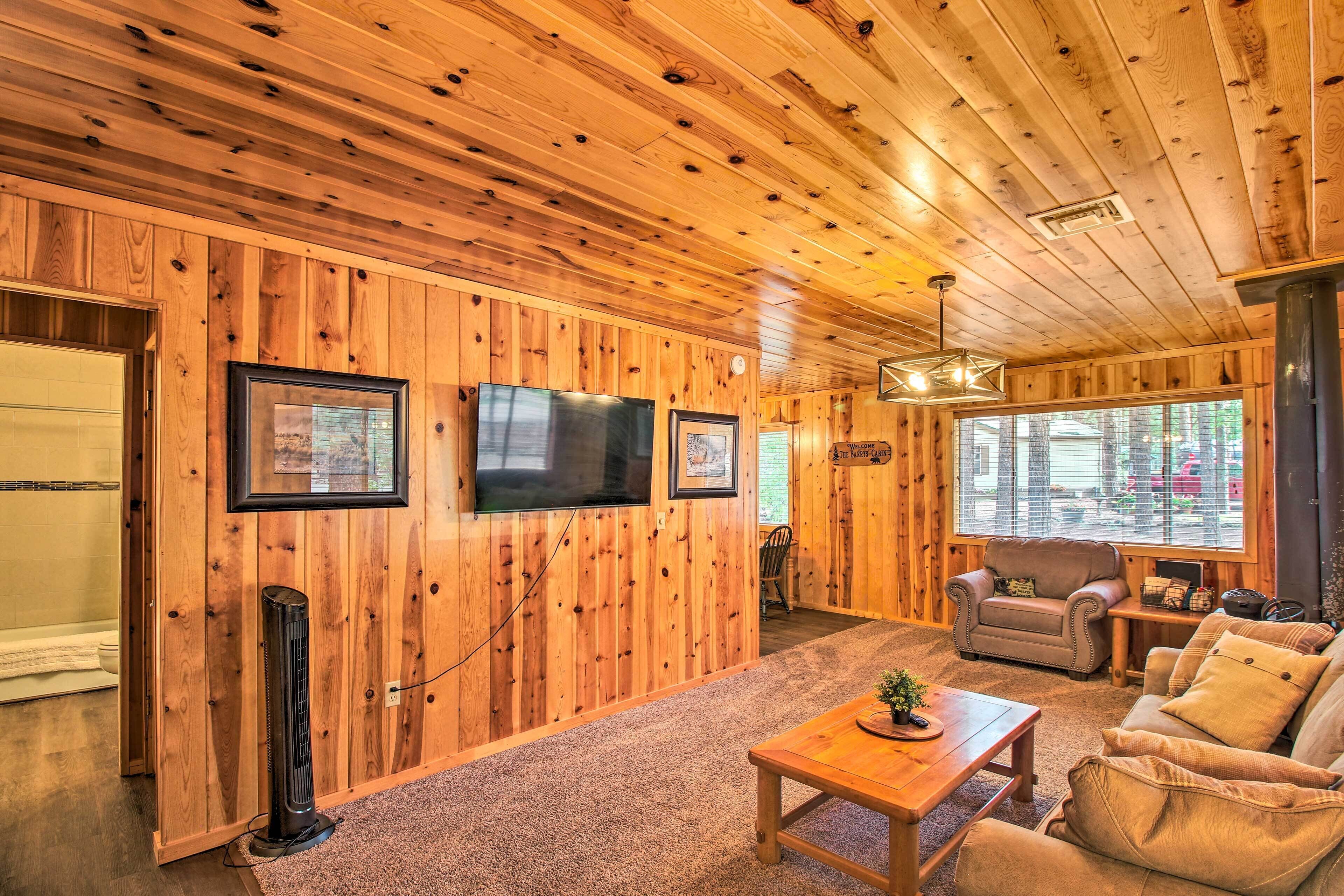 A cozy cabin interior with wooden walls, a TV mounted on the wall, a comfortable sofa, and a small table.