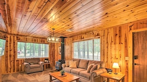 Ein gemütliches Blockhaus-Interieur mit Holzbalkendecke, einer Couch, einem Zweisitzer-Sofa, einem Couchtisch und einem Kamin.