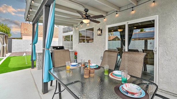 Patio esterno con tavolo in vetro, sedie e ventilatore a soffitto.