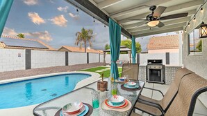 Patio esterno con tavolo in vetro apparecchiato per mangiare, piscina e zona barbecue.