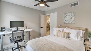 Una camera da letto con un letto, una scrivania con un computer, una ventola a soffitto e una porta che conduce al bagno.