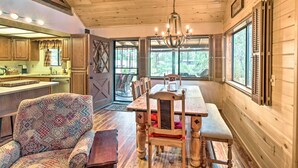 A wooden interior with a dining table, chairs, a patterned armchair, and a chandelier. - Rustic, Forest-view Retreat in Heber-overgaard! (Overgaard)