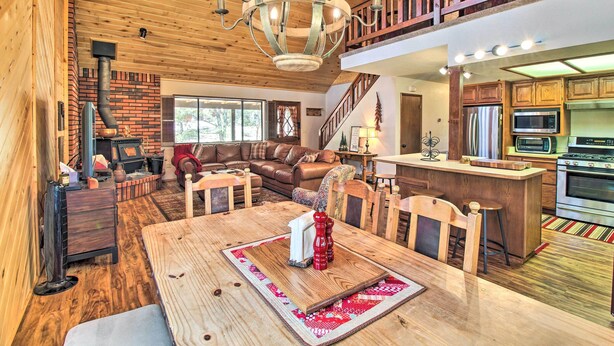 A spacious living area with a wooden ceiling, a fireplace, a dining table with chairs, a kitchen with modern appliances, and a staircase leading to an upper level. - Rustic, Forest-view Retreat in Heber-overgaard! (Overgaard)