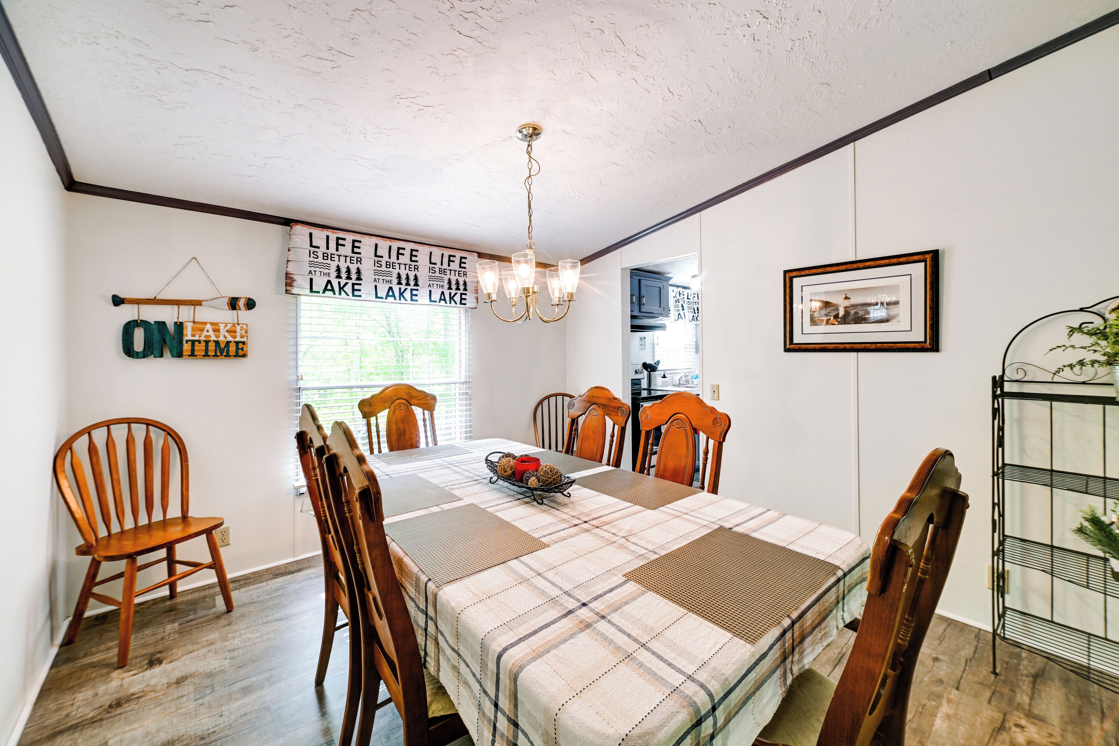 A dining room with a table set for four, wooden chairs, a chandelier, and a window with blinds.