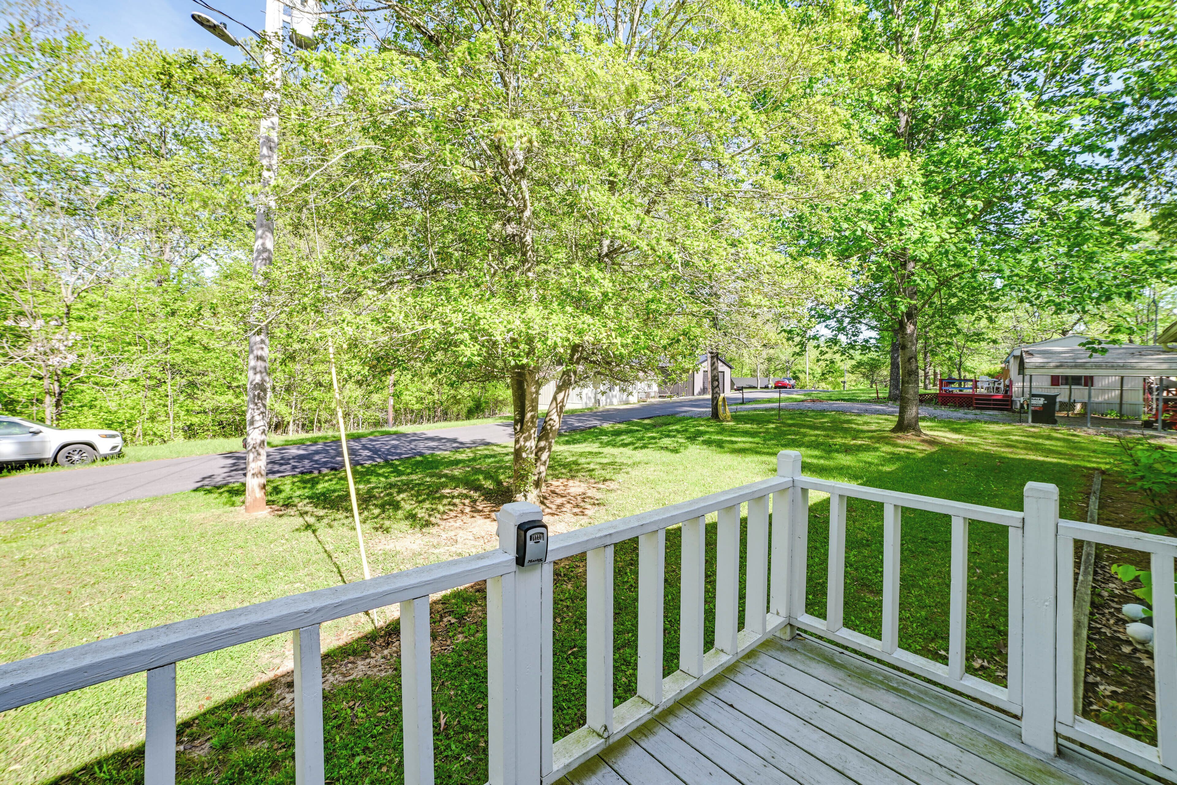 Une terrasse en bois avec une balustrade blanche, entourée d’herbe verte et d’arbres.