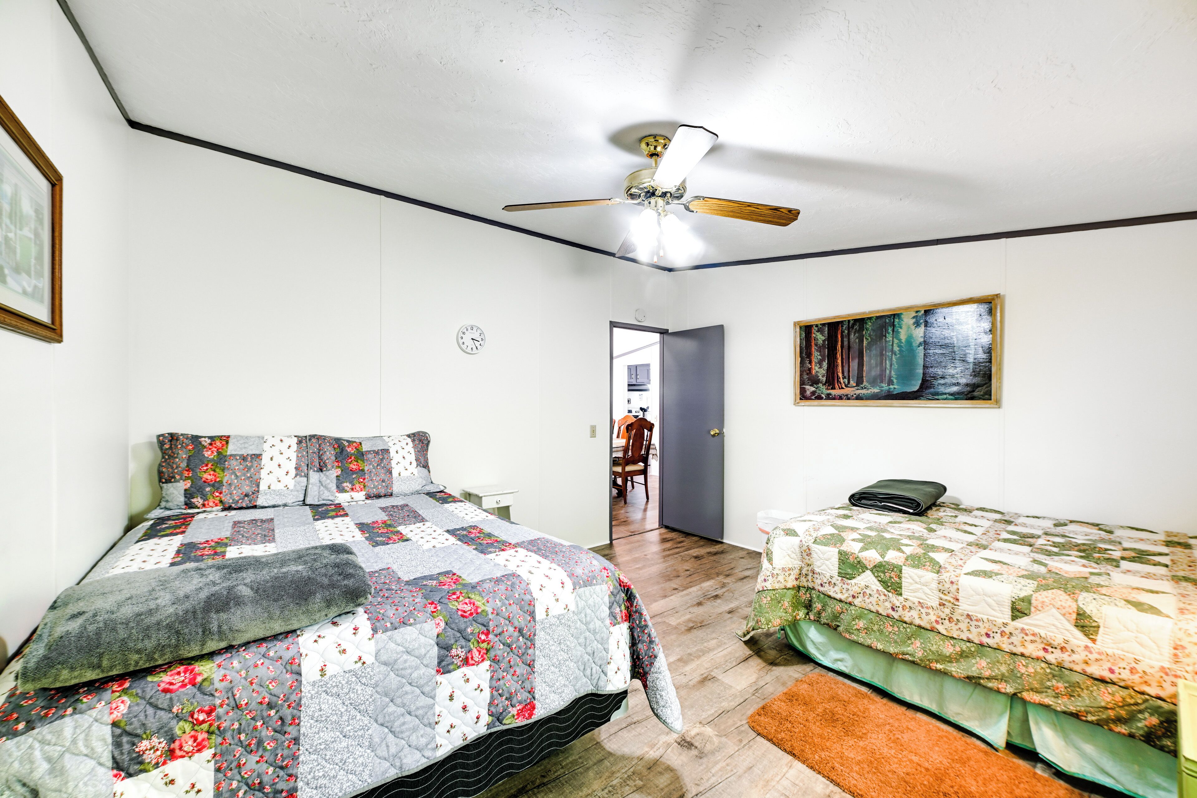 Un dormitorio con una cama, una cama individual, un ventilador de techo, un cuadro y una puerta que da a otra habitación.