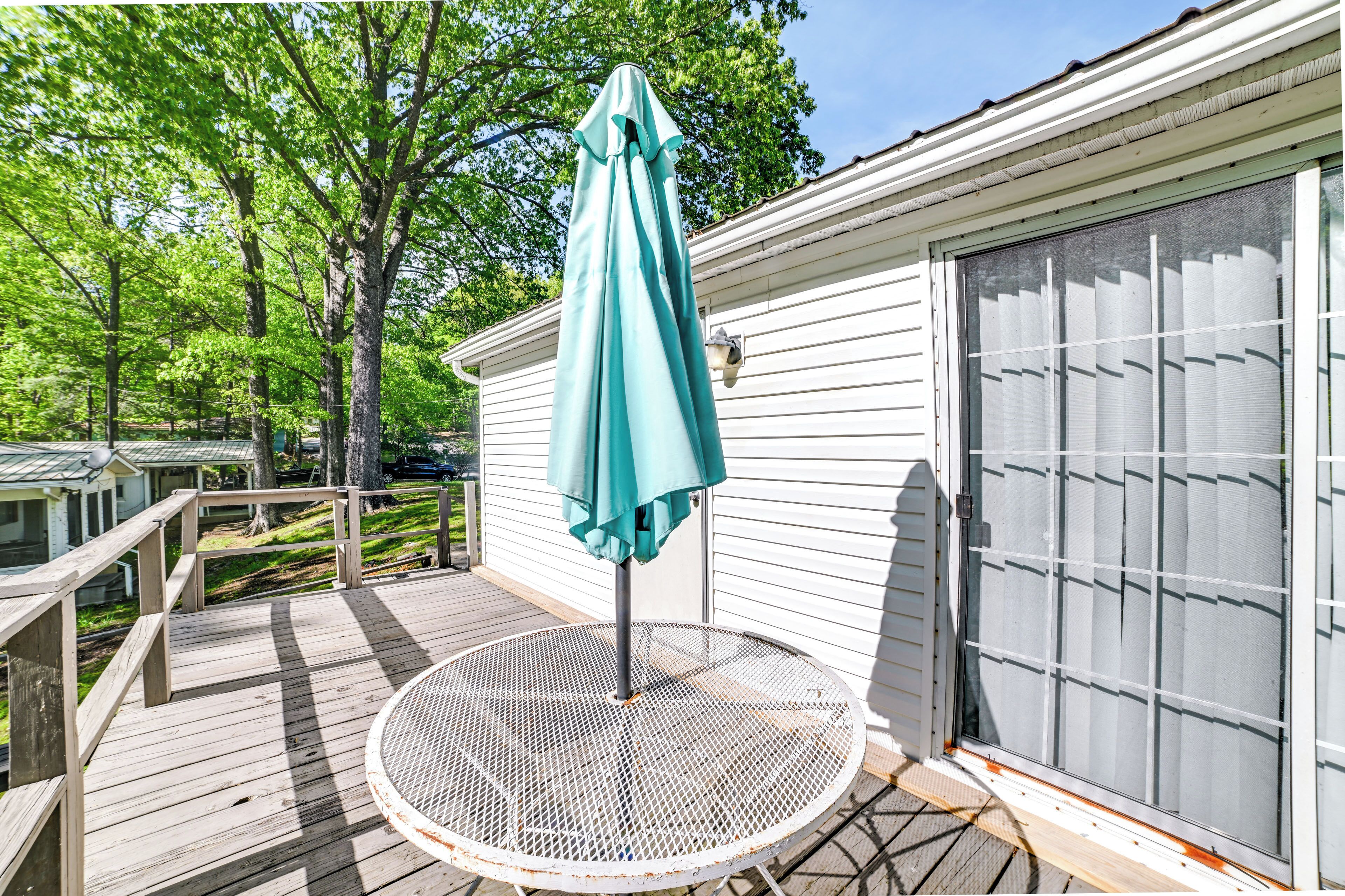 A wooden deck with a metal table and a teal umbrella.