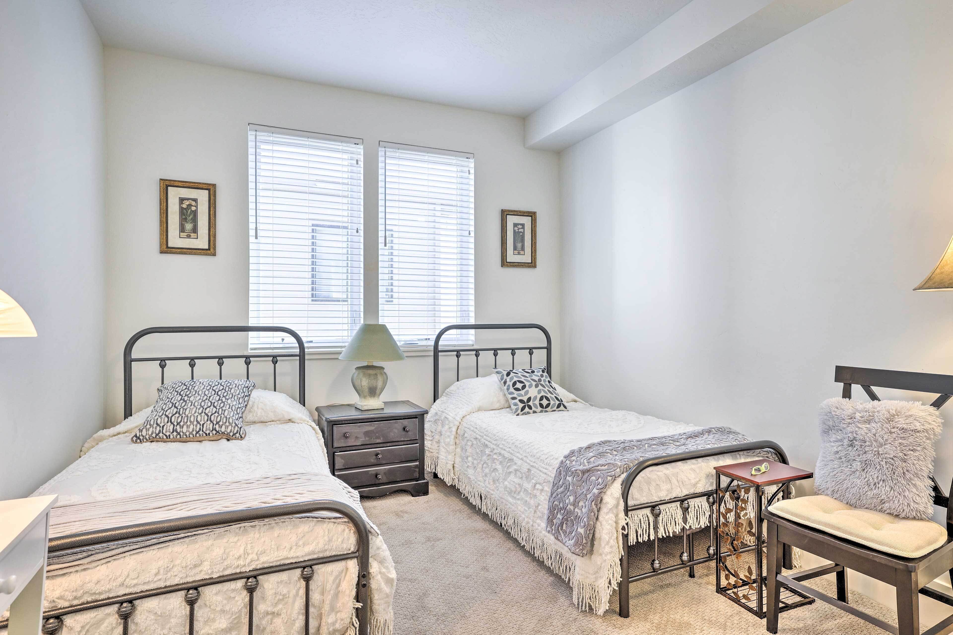 A bedroom with two beds, a chair, a nightstand, and two windows.