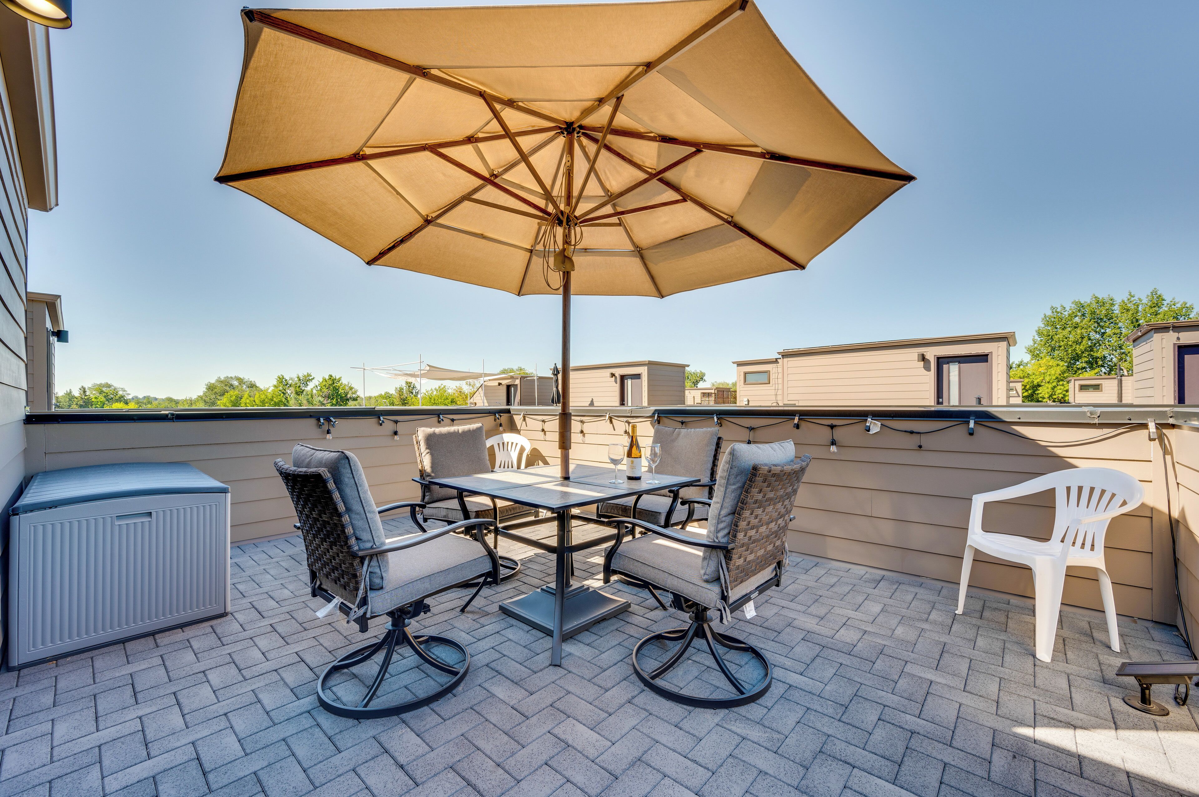 Une terrasse extérieure avec une table et des chaises, un grand parasol et une chaise en plastique blanche.