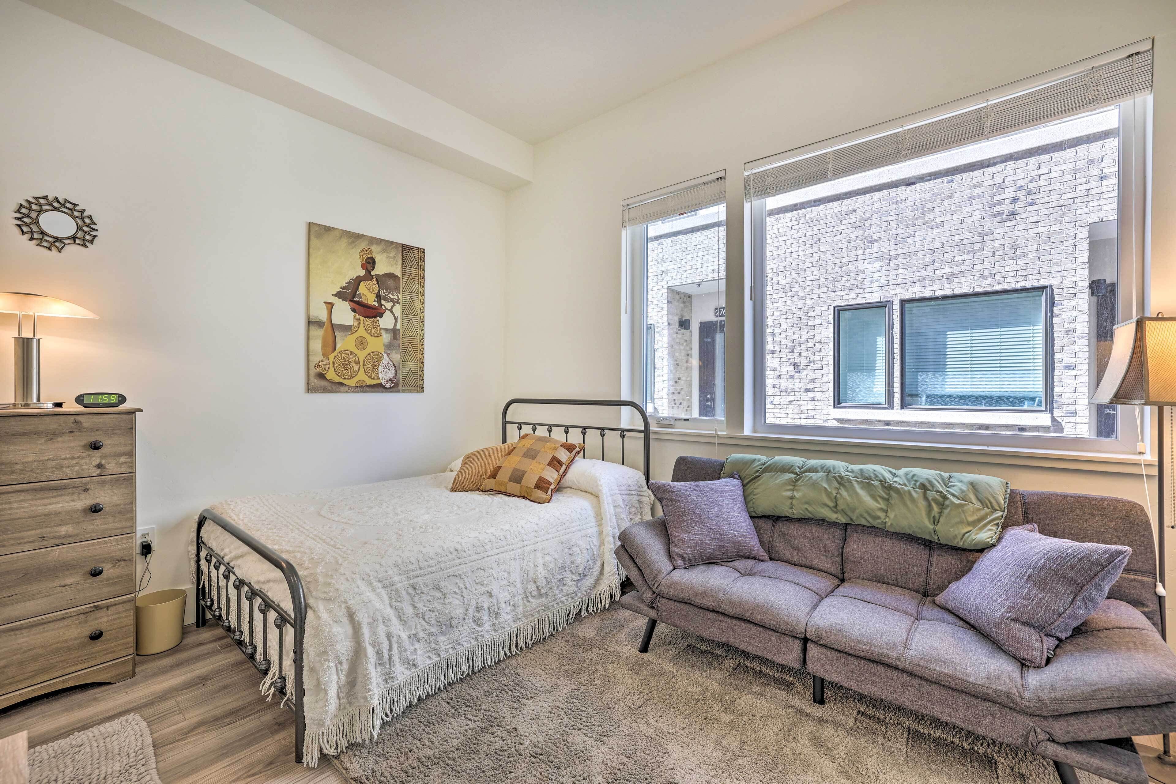Une chambre à coucher comprenant un lit, un canapé, une commode, une fenêtre avec des stores et une œuvre d’art accrochée au mur.