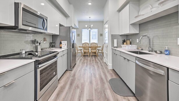 A modern kitchen with stainless steel appliances, white cabinetry, and a wooden dining table with chairs. - Boise Townhome w/ Rooftop Deck, 2 Mi to Downtown! (Boise)
