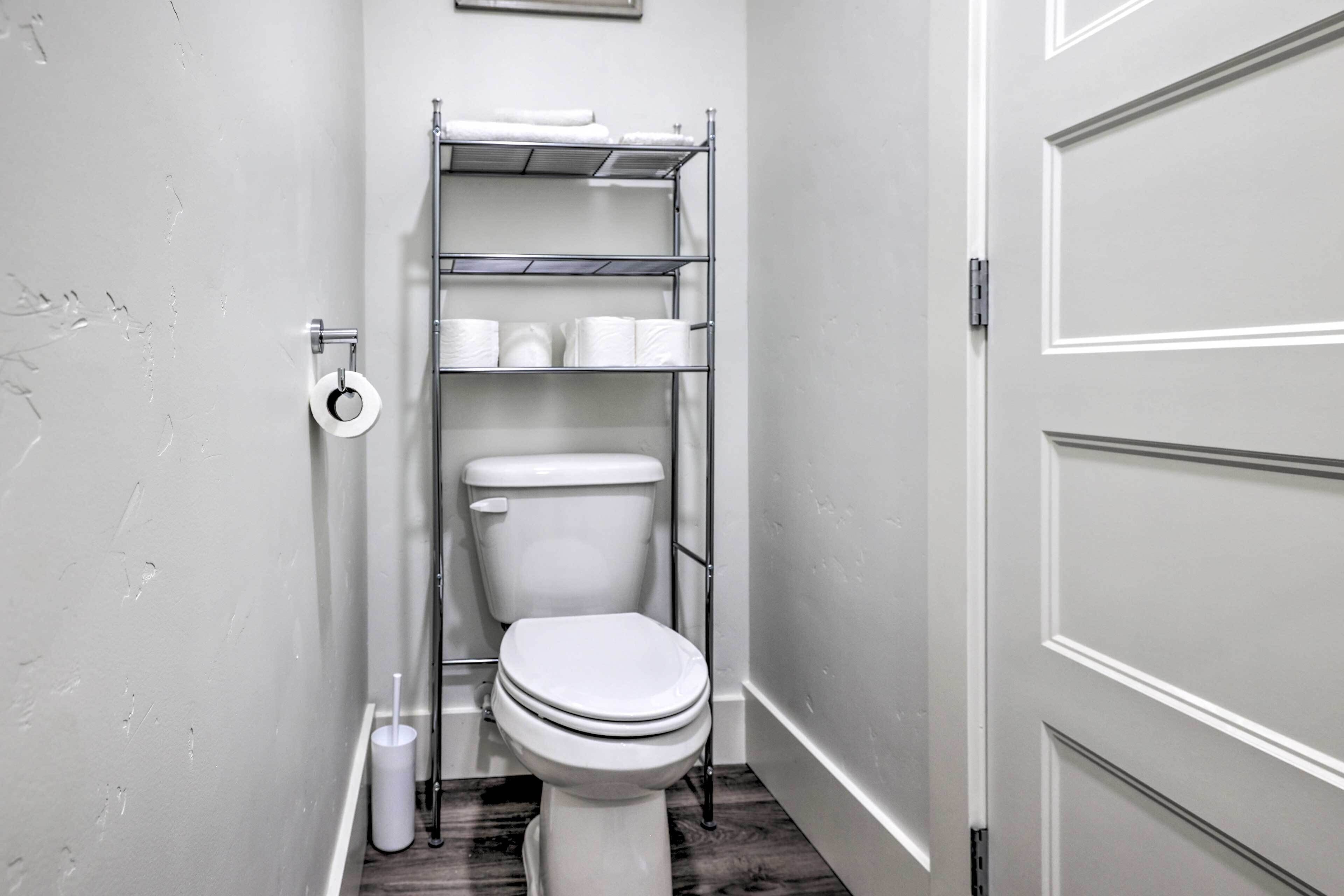 Un baño con inodoro, un estante con artículos de aseo y un rollo de papel higiénico en la pared.