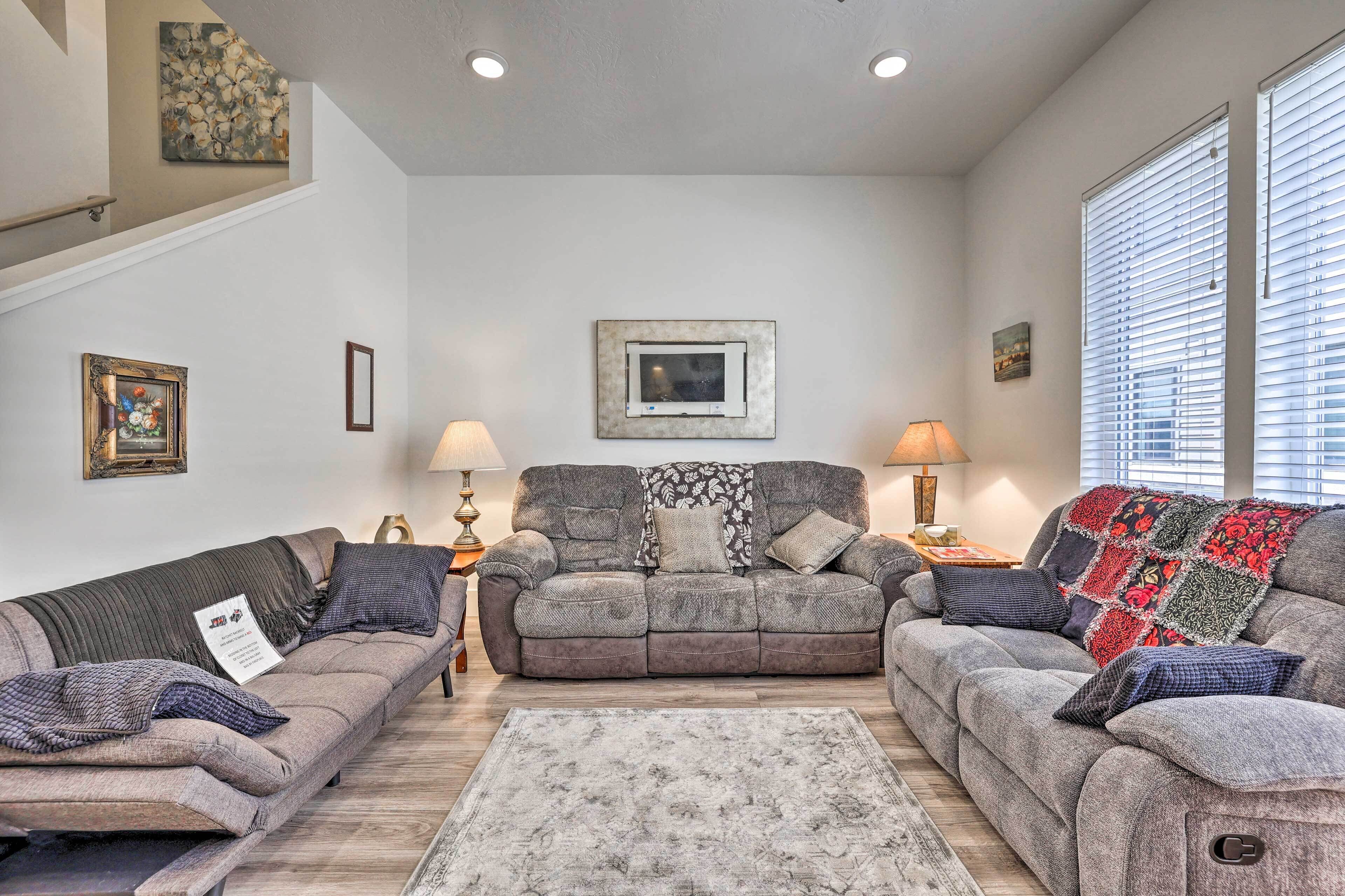 A living room with two sofas, a coffee table, and a rug. There are two lamps, a painting on the wall, and a window with blinds.