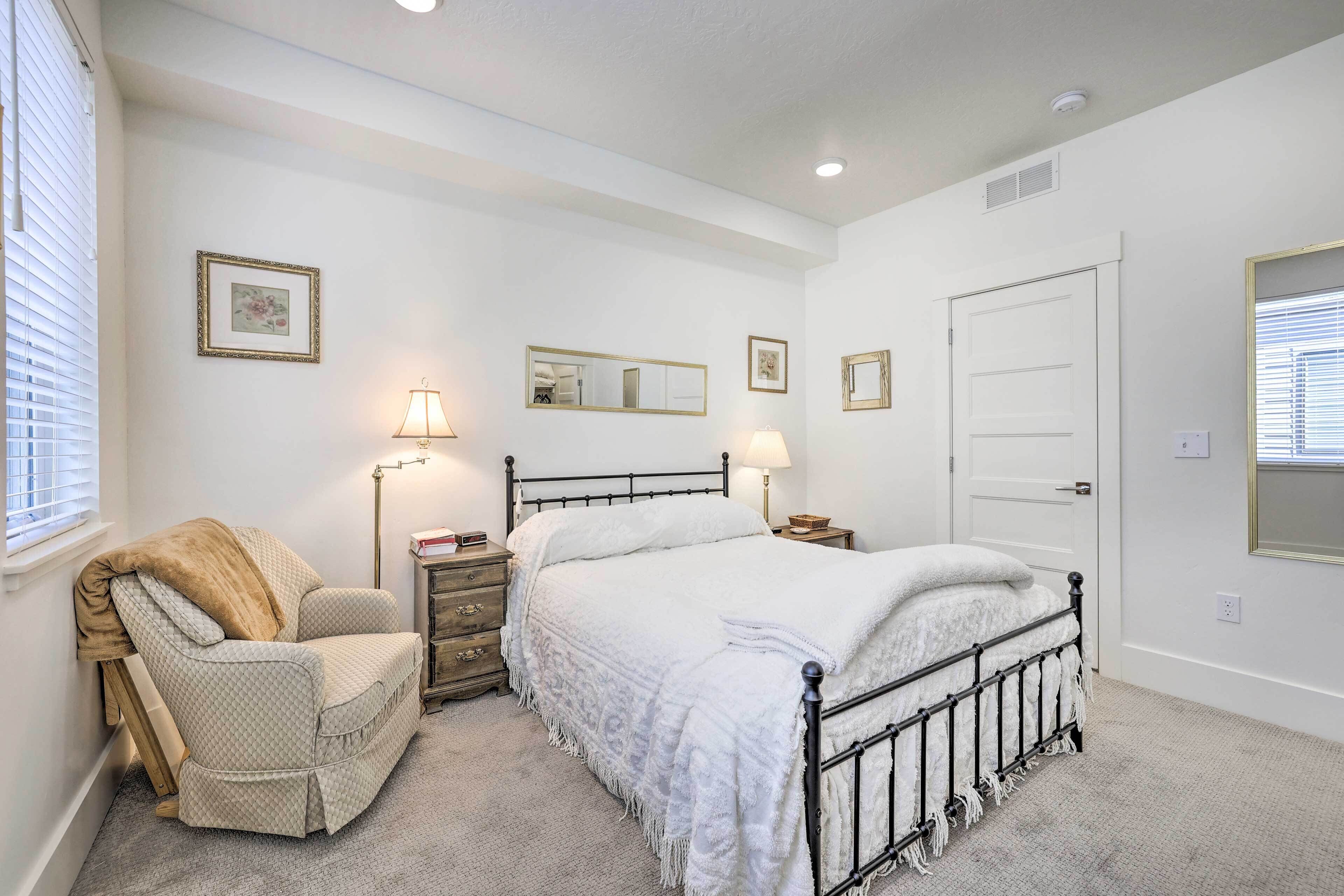 A bedroom with a bed, a chair, a nightstand, a lamp, and a door.