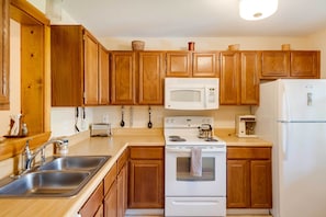 A kitchen with wooden cabinets, stainless steel sinks, a white stove, a microwave, and a refrigerator. - Lovely White Mountains Condo: Hike, Ski & Unwind! (Lincoln)