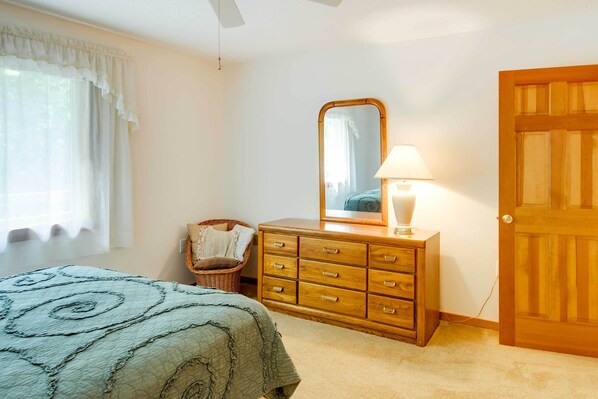 A bedroom with a bed, a dresser, a mirror, a lamp, and a door. - Lovely White Mountains Condo: Hike, Ski & Unwind! (Lincoln)