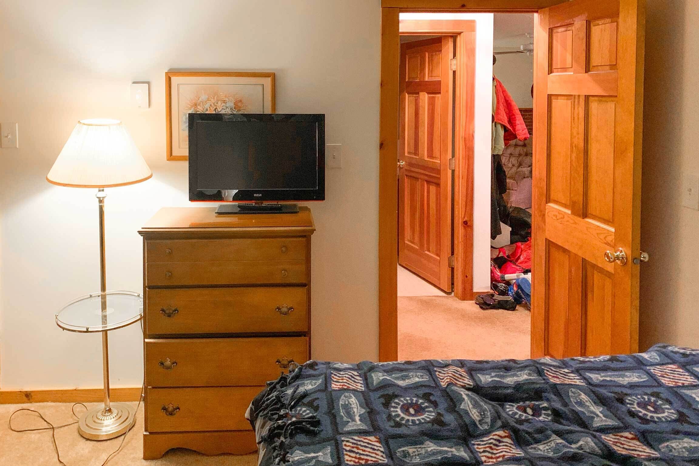 A bedroom with a bed, a dresser, a television on top, a lamp, and a closet.