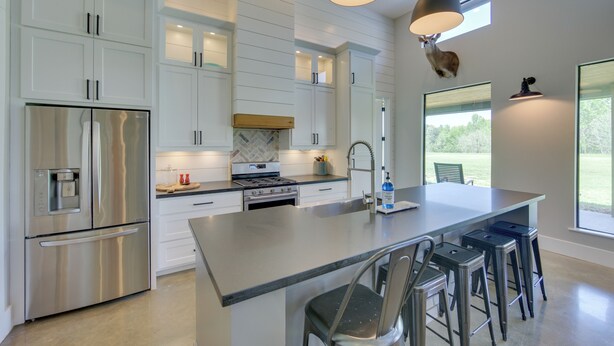 A modern kitchen with white cabinetry, stainless steel appliances, and a central island with bar stools.