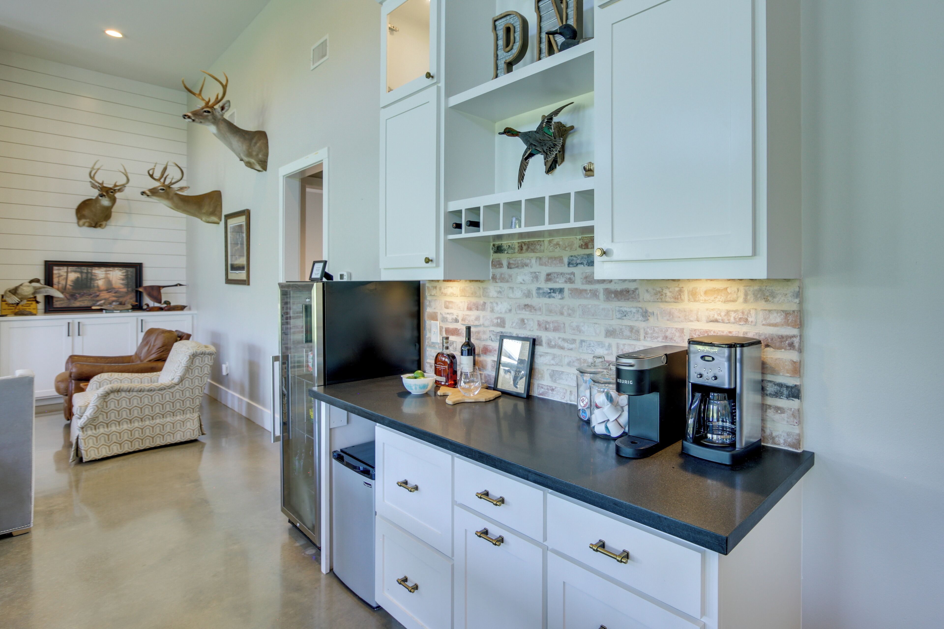 A kitchen with white cabinets, a coffee maker, and mounted animal heads.