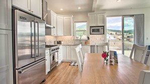 A modern kitchen with stainless steel appliances, white cabinetry, and a wooden dining table. - Exquisite Discovery Mtn Home w/ Sweeping Views! (Philipsburg)