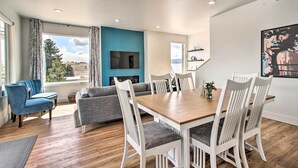 A modern living room with a wooden dining table, white chairs, a grey sofa, and a blue accent wall. - Exquisite Discovery Mtn Home w/ Sweeping Views! (Philipsburg)