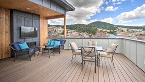 A wooden deck with outdoor furniture, a flat-screen TV, and a view of a town and mountains. - Exquisite Discovery Mtn Home w/ Sweeping Views! (Philipsburg)