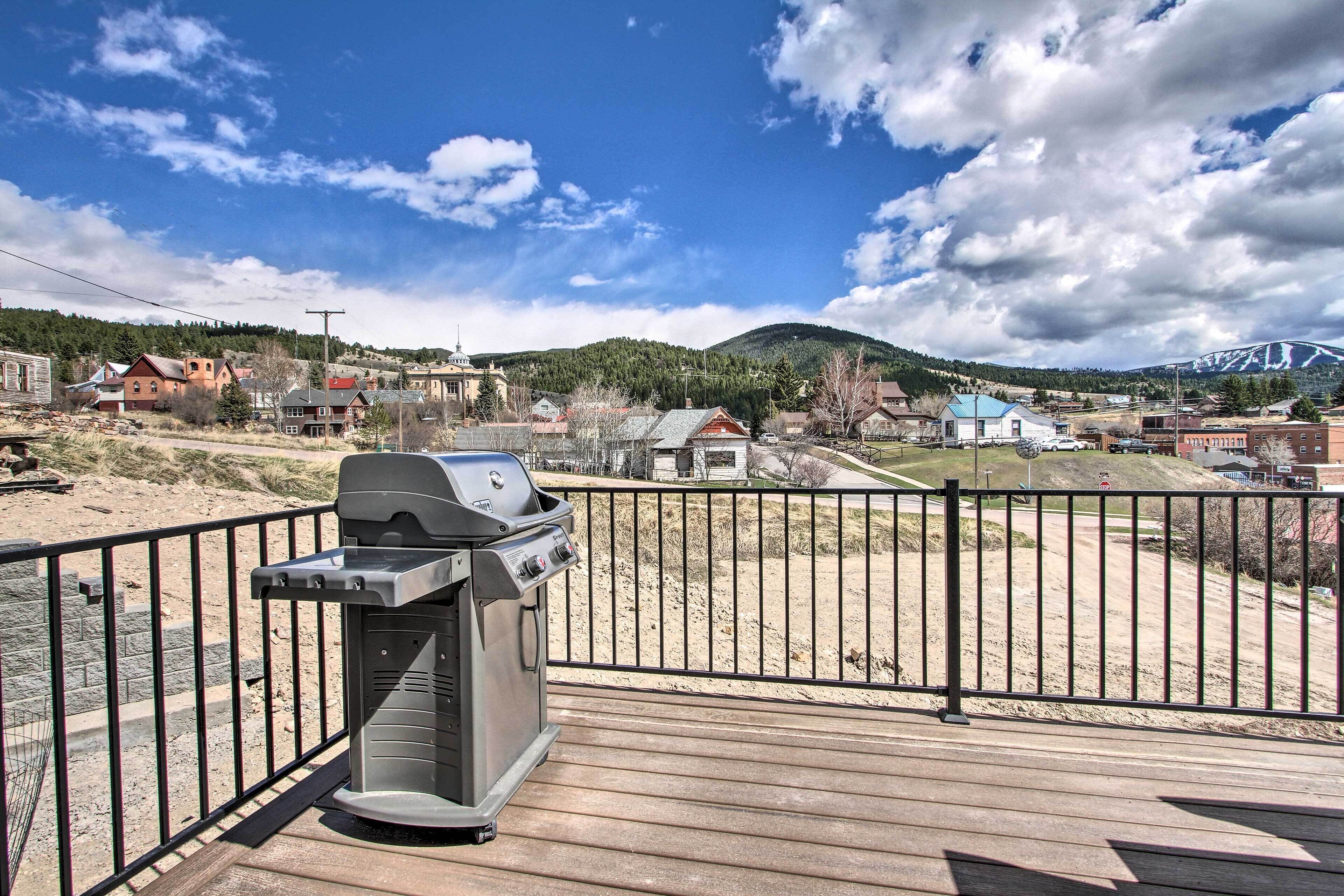 A barbecue grill on a wooden deck with a view of a town and mountains in the background.