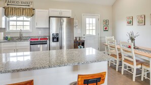 Een keuken met een granieten aanrecht, witte kasten, een roestvrijstalen koelkast, en een eethoek met houten stoelen en een tafel.